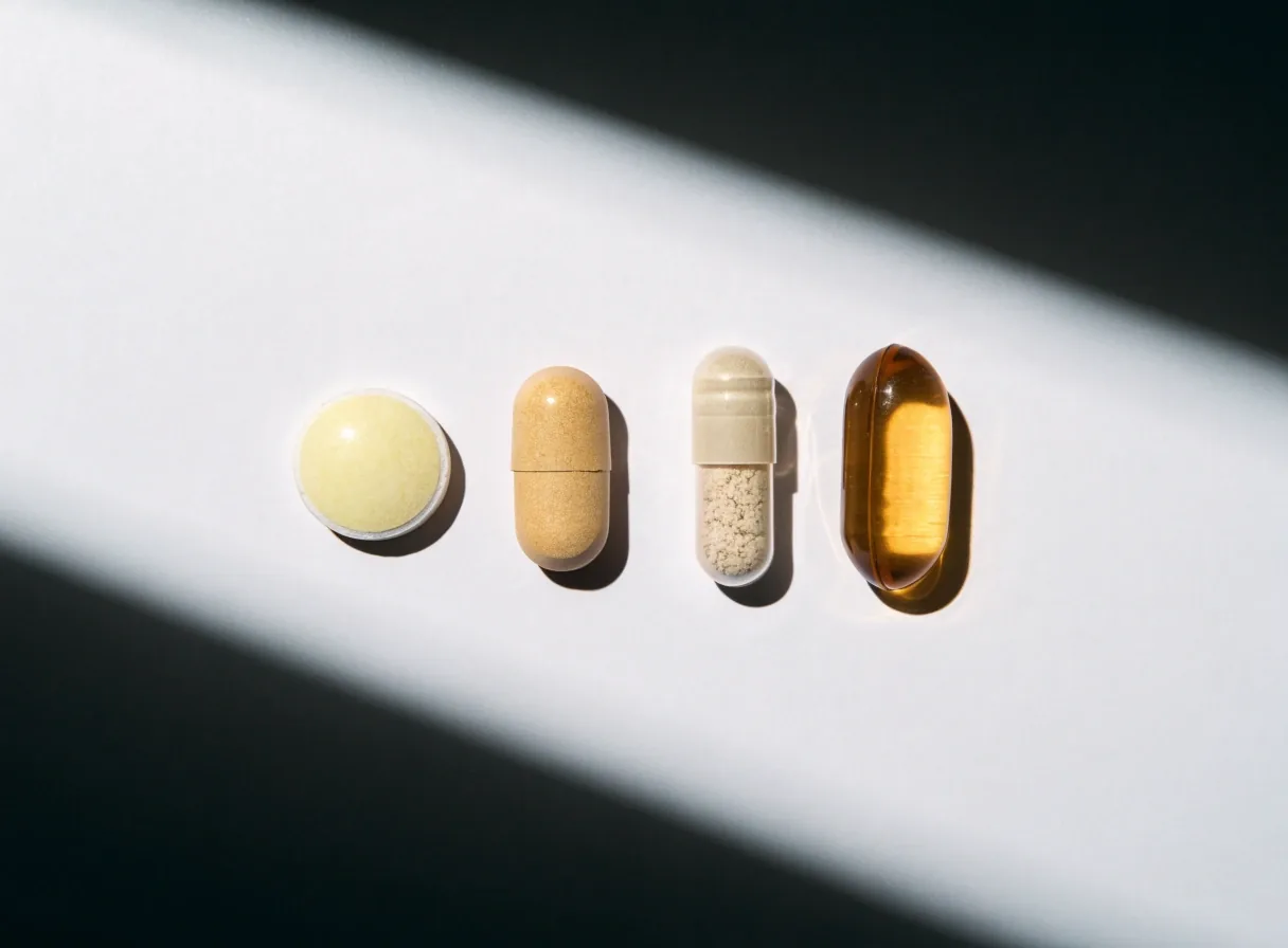 A row of mixed formats — tablet, caplet, capsule and softgel — laid in a straight line on white stock